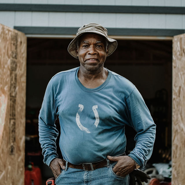 Man with his hands on his hips smiling at camera standing outside his shed.